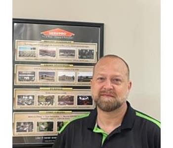 Man in green and black shirt stands in front of framed picture