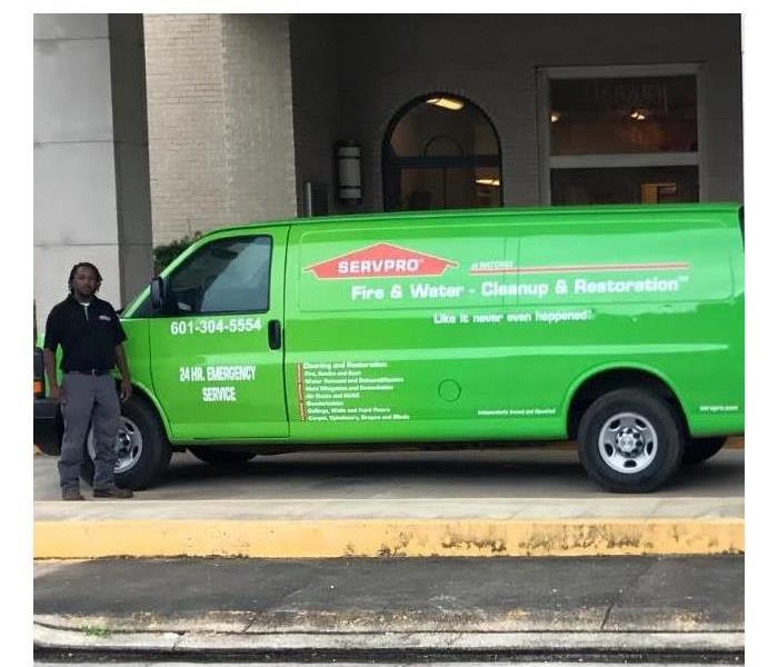 Team member standing in front of green SERVPRO van at water loss site